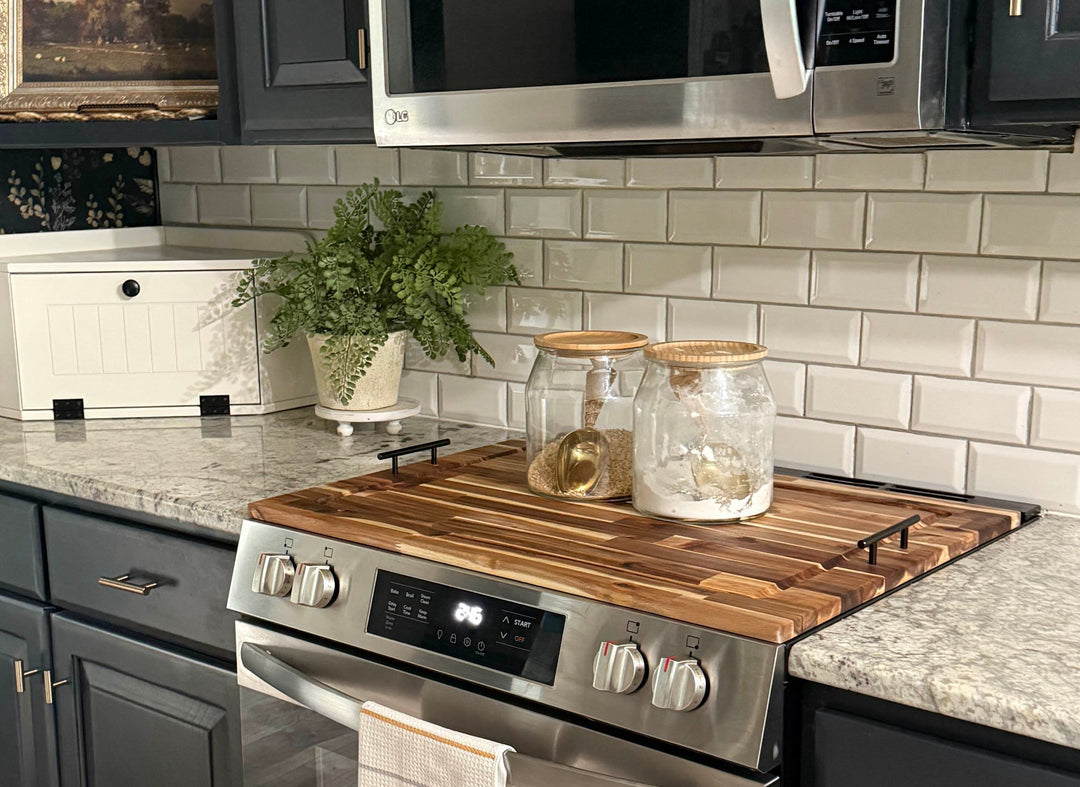 A modern kitchen corner featuring dark charcoal gray cabinets, a white subway tile backsplash, a stainless steel gas range with a wooden cooktop, and a built-in stainless steel microwave.