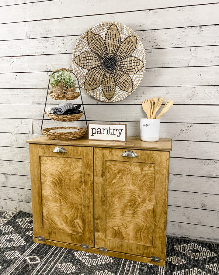 Golden oak double size tilt out trash bin.  Handle options are gold, silver, or black. Panel options are cedar look panel, chalkboard, barn metal, or flat front.