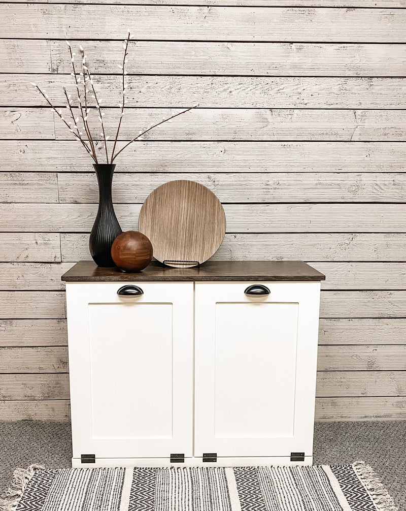 White tilt out double trash bin.  Handle options are gold, silver, or black. Panel options are cedar look panel, chalkboard, barn metal, or flat front.