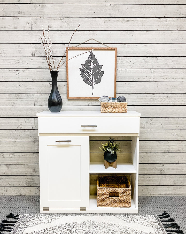 White tilt out trash bin with a shelf and drawer.  Handle options are gold, silver, or black. Panel options are cedar look panel, chalkboard, barn metal, or flat front.